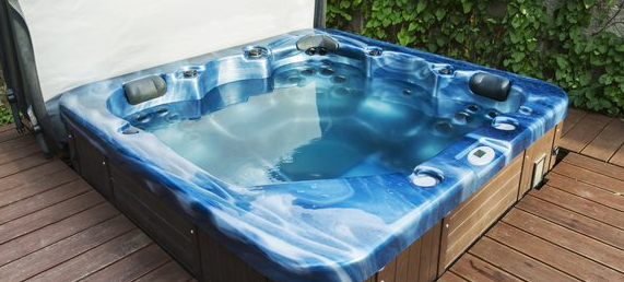 The image shows a blue and white marbled hot tub or spa installed on a wooden deck next to some greenery.